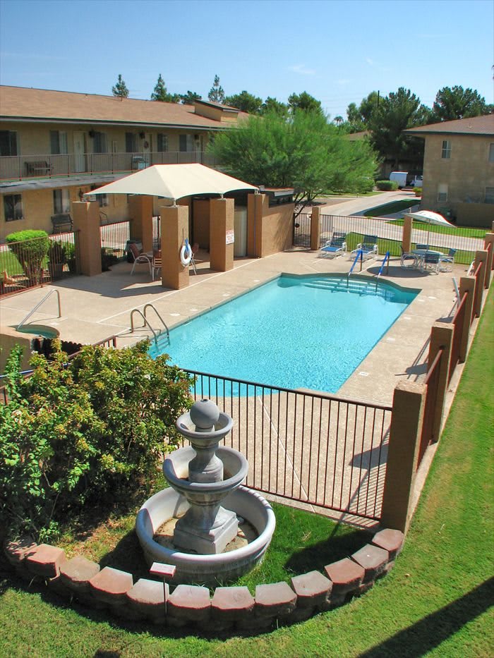 An outdoor swimming pool area with a gazebo and fountain within an apartment complex.