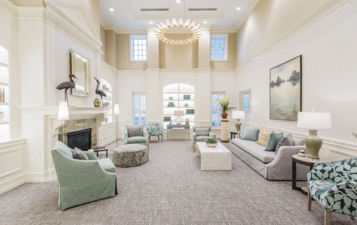 A spacious and elegantly decorated living room featuring modern furniture, a chandelier, large windows, and a fireplace.