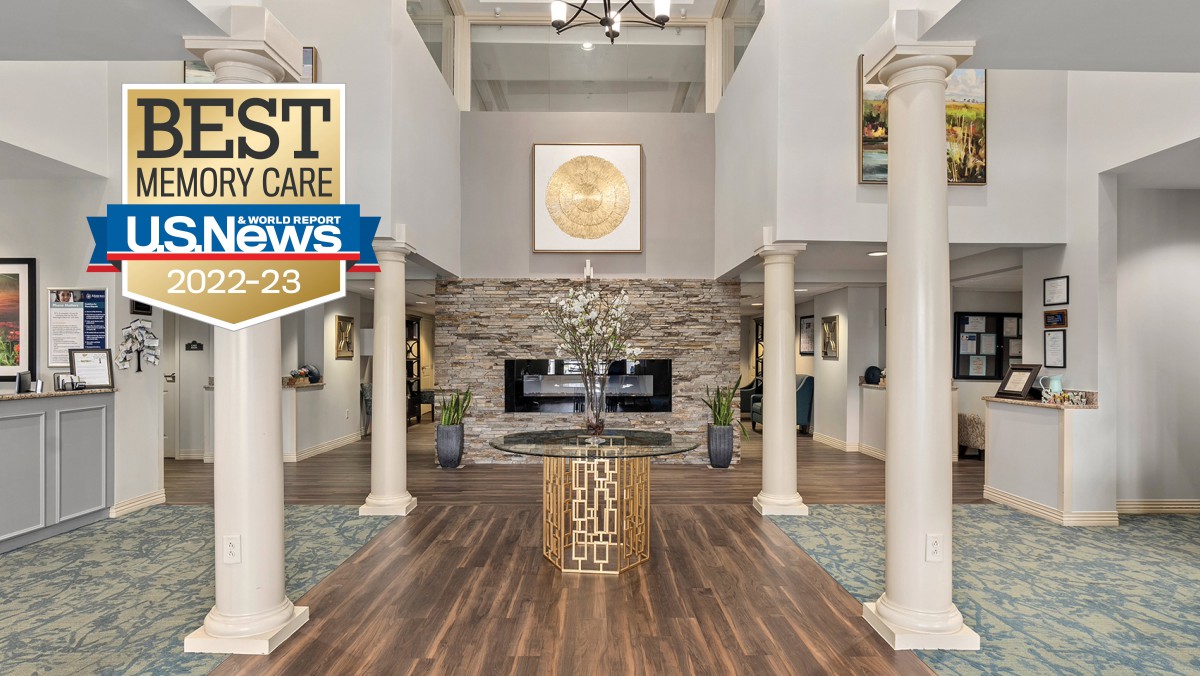 A modern and elegant lobby featuring a fireplace, wooden flooring, and decorative columns. An award emblem is displayed in the upper left corner.