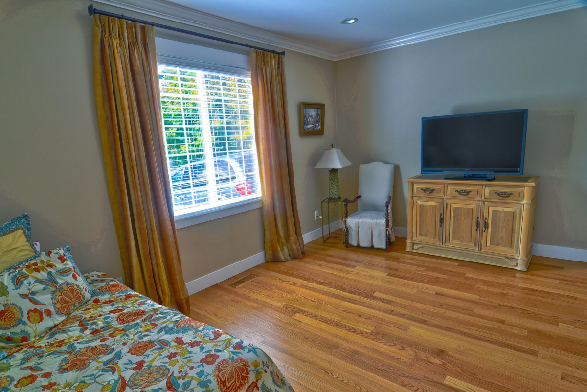 A cozy bedroom with a TV, window with curtains, and wooden flooring.