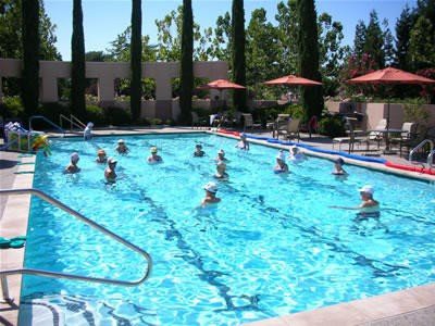 A group of people participating in a water aerobics class in an outdoor swimming pool.
