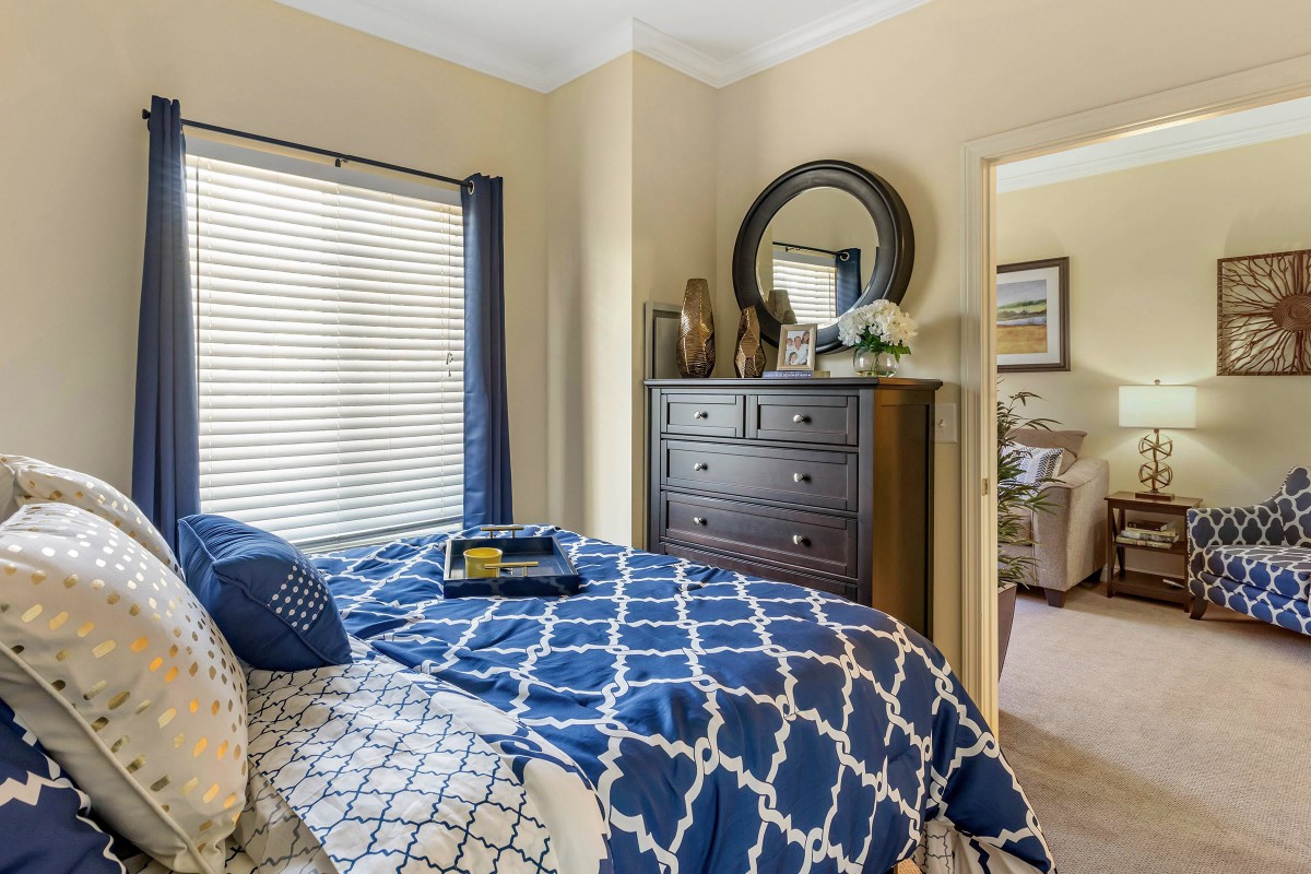 A cozy bedroom with blue patterned bedding and a wooden dresser topped with decorative items.