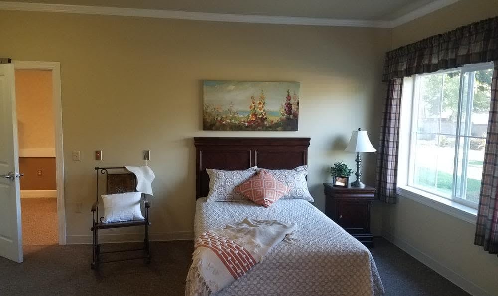 A cozy bedroom with a neatly made bed, a lamp on the nightstand, and artwork above the headboard.