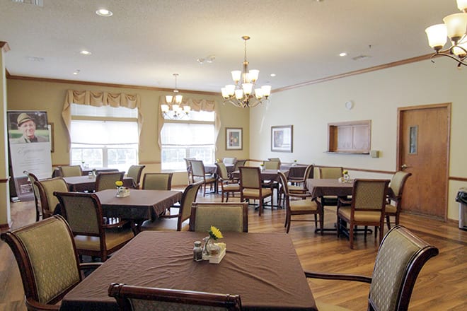 A spacious dining room with multiple tables and chairs, featuring elegant chandeliers.