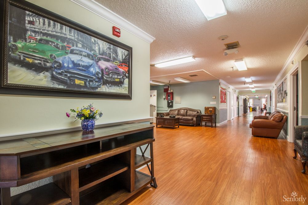 A well-lit hallway featuring wooden floors, artwork on the walls, and neatly arranged furniture.