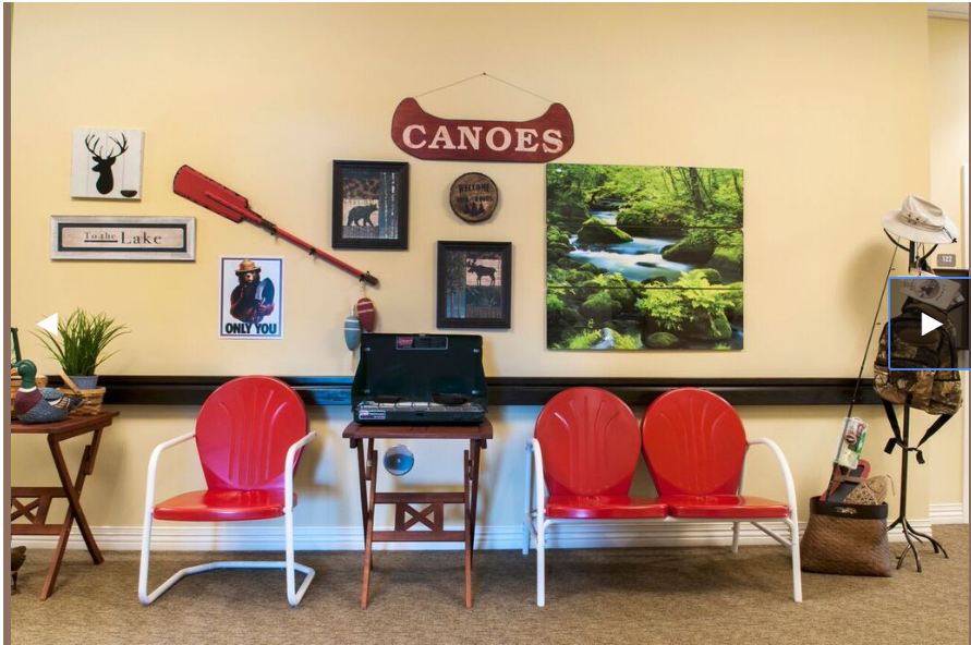 A waiting area with red chairs and a canoe-themed wall, featuring decorative paddles, photo frames, a nature painting, and a computer station.