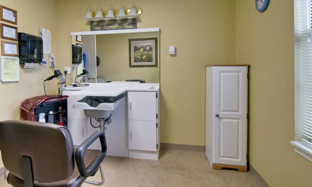 An interior view of a hair salon with a chair, sink, and cabinet.