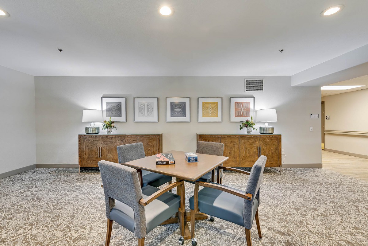 A cozy lounge area featuring a table with four chairs, decorative artwork, and sideboards adorned with lamps.