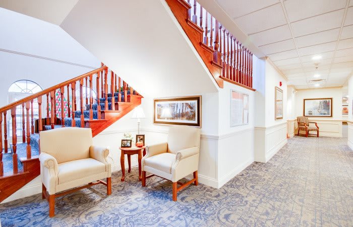 A cozy hallway with upholstered chairs and a staircase featuring wooden railings.