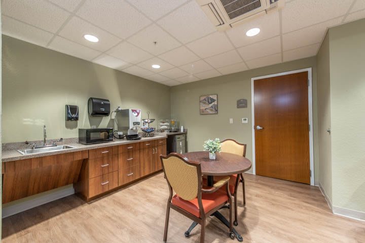 A cozy break room with a kitchenette, featuring a small table and chairs, wooden cabinets, and appliances like a microwave and coffee maker.