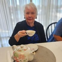 An elderly woman enjoying a cup of tea at a table indoors.