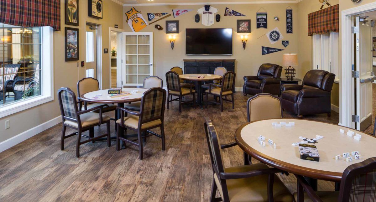 A cozy dining room with multiple tables and chairs, decorated with sports pennants and a large TV on the wall.