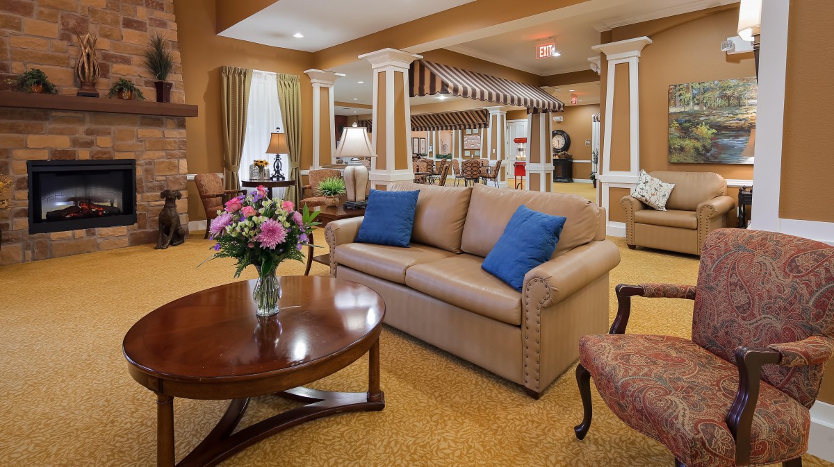 A cozy living room with a sofa, coffee table, and floral arrangement, featuring warm decor and elegant columns.