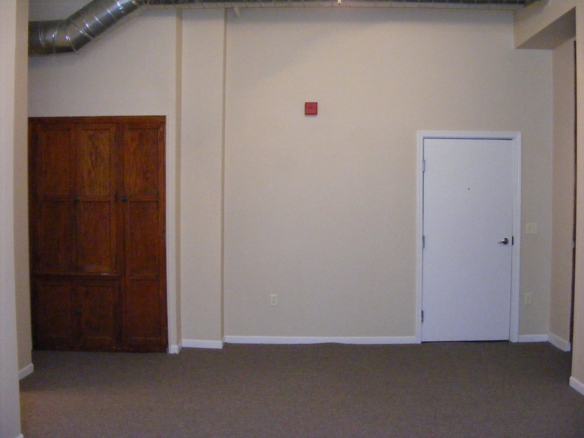 An empty room with two doors, one wooden and one white, on a carpeted floor.