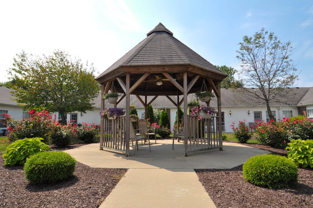 A wooden gazebo surrounded by a landscaped garden with flowers and well-kept pathways.