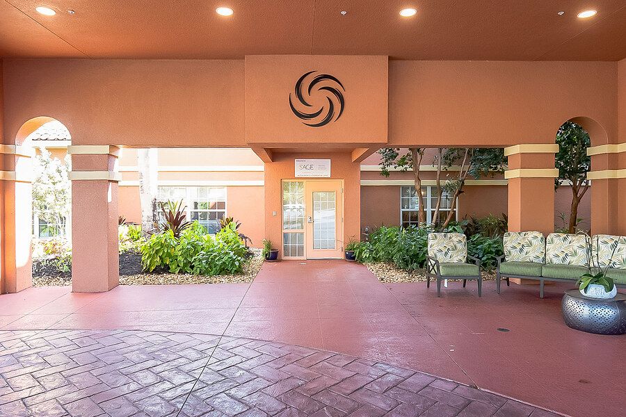 The image shows an entrance area with outdoor seating, featuring plants and distinctive architectural design.