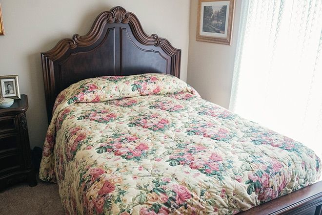 A vintage-style bedroom featuring a bed with a floral patterned quilt and an ornate wooden headboard.