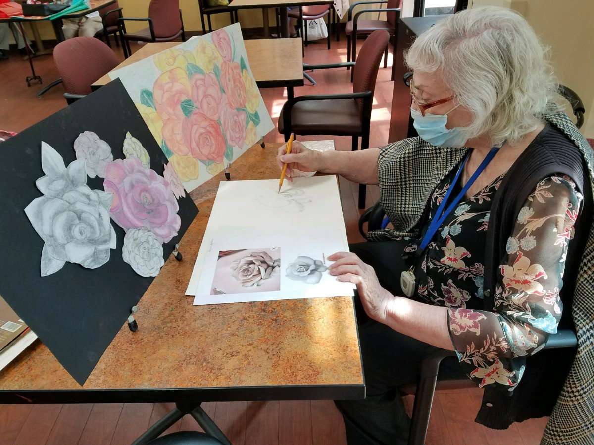 A woman engaged in painting flowers at an indoor art session.