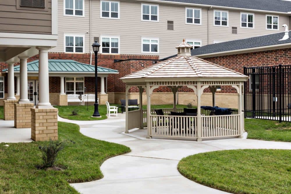 A community outdoor area featuring a gazebo and pathways surrounded by green grass, adjacent to a building.