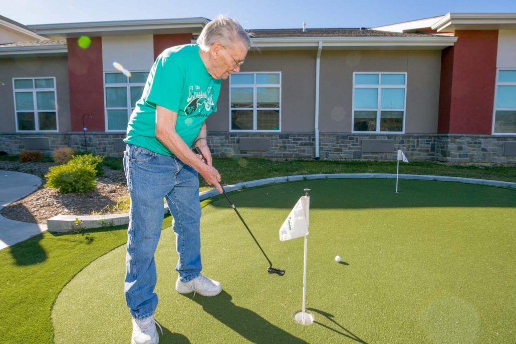 A senior man practicing putting on an outdoor mini-golf course.