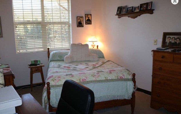 A cozy bedroom with a single bed, decorated with floral bedding and illuminated by a bedside lamp.