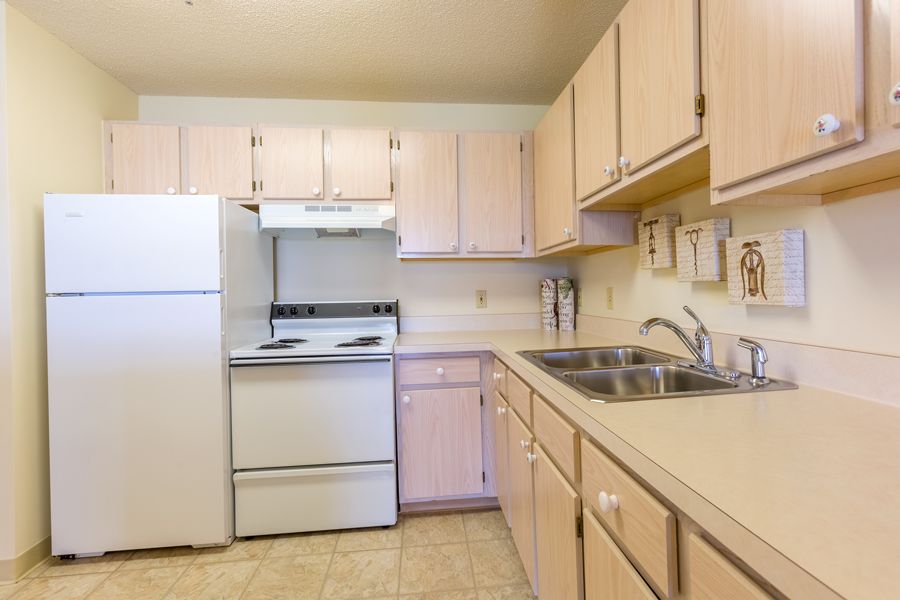 A small kitchen featuring light-colored cabinets, a refrigerator, stove, and double sink.