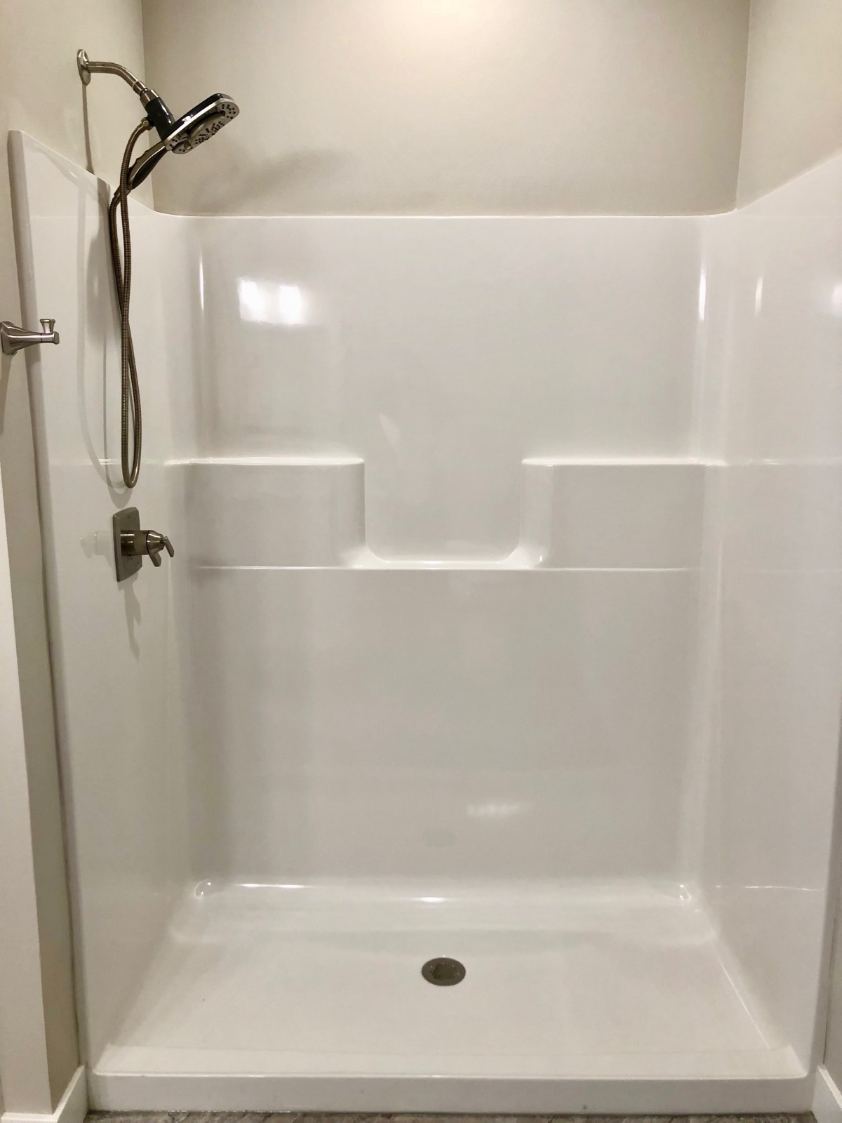 A clean white shower with built-in shelves and a showerhead.