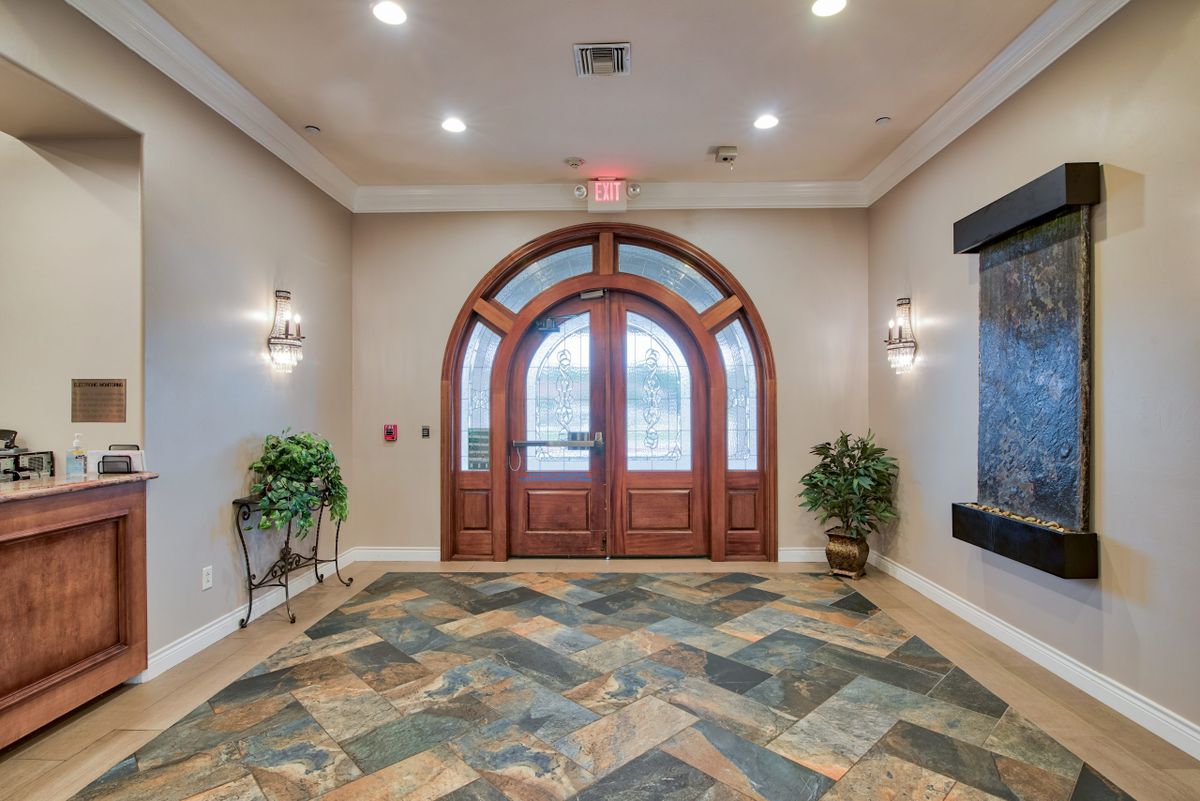A well-lit interior entrance with an arched wooden door and tile flooring, accented by plants and wall sconces.