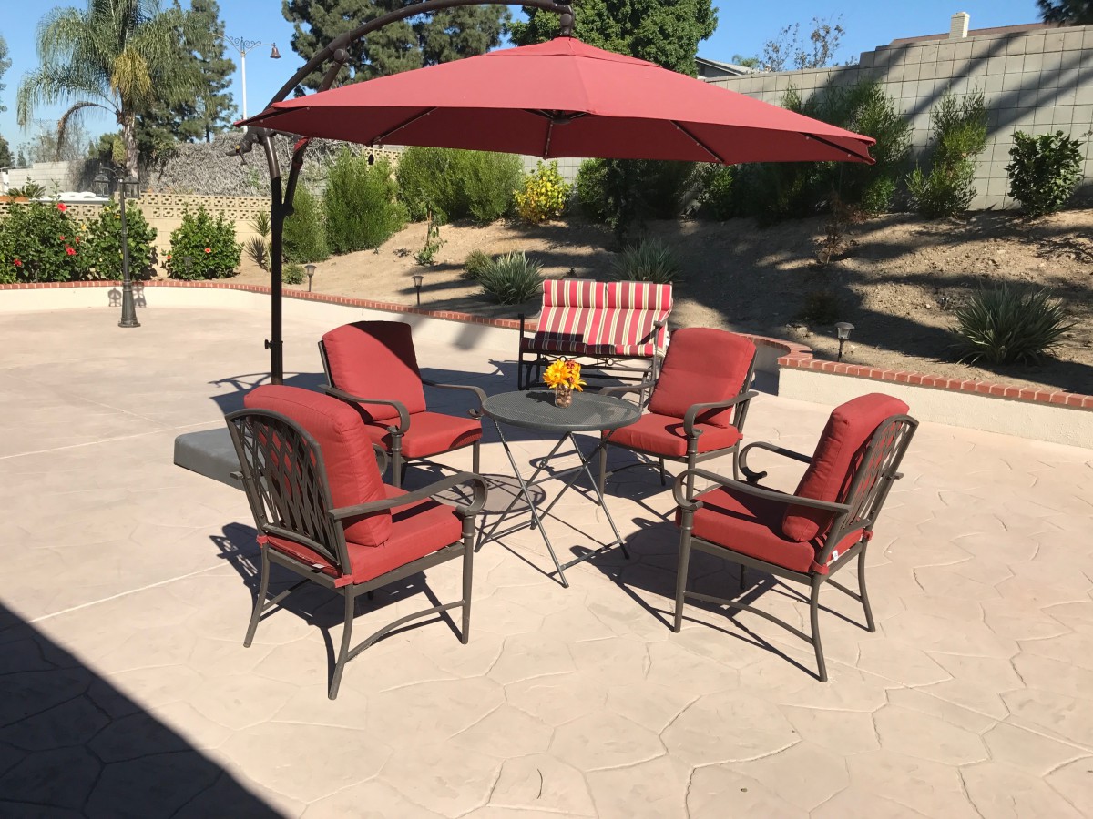 A patio setup with red cushioned chairs, a table, and a large umbrella on a sunny day.