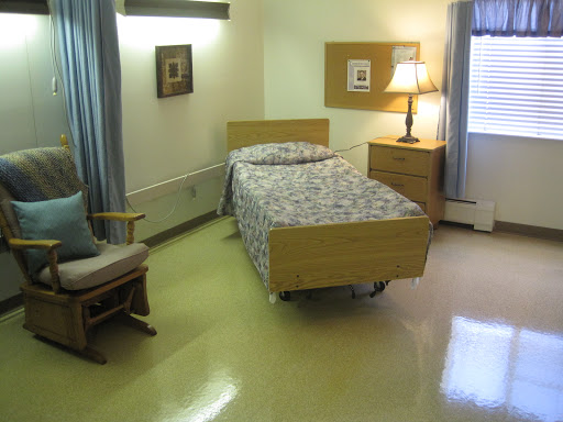 A simple and functional hospital room featuring a single bed, a chair, and a lamp.