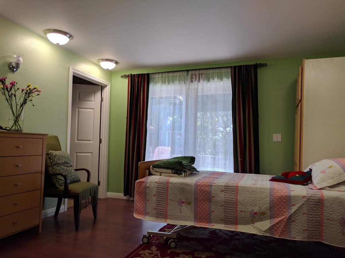 A cozy bedroom with green walls, a bed near the window, and a comfortable chair.