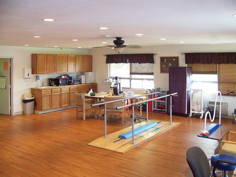 A spacious rehabilitation room equipped with parallel bars and a kitchenette for physical therapy sessions.