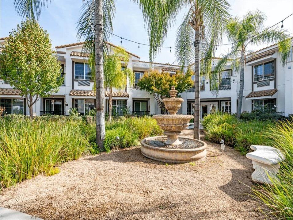 A beautiful house with a central courtyard featuring a multi-tiered fountain surrounded by palm trees and lush garden landscaping.