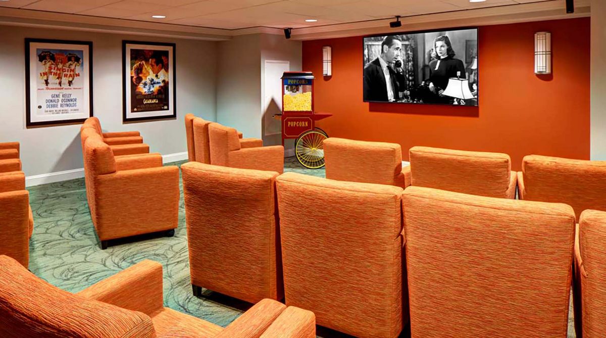 A cozy home theater room with orange seating and a large screen playing a classic black-and-white movie.