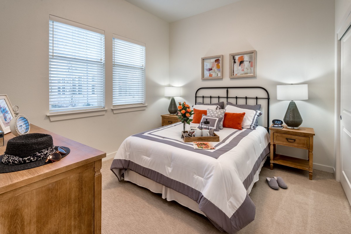A cozy bedroom with a neatly made bed, adorned with pillows and surrounded by wooden furniture and decorative artwork.