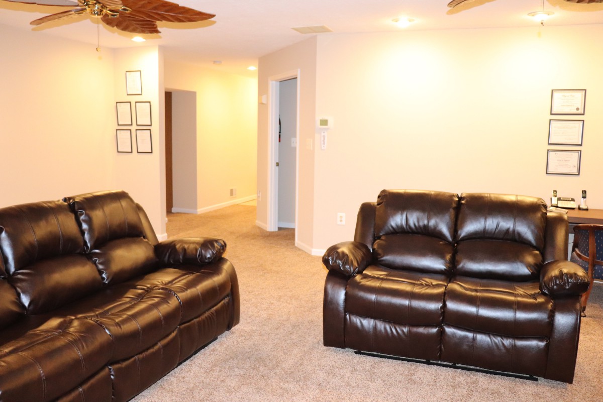A cozy living room featuring two comfortable leather sofas and a carpeted floor, leading to a hallway.