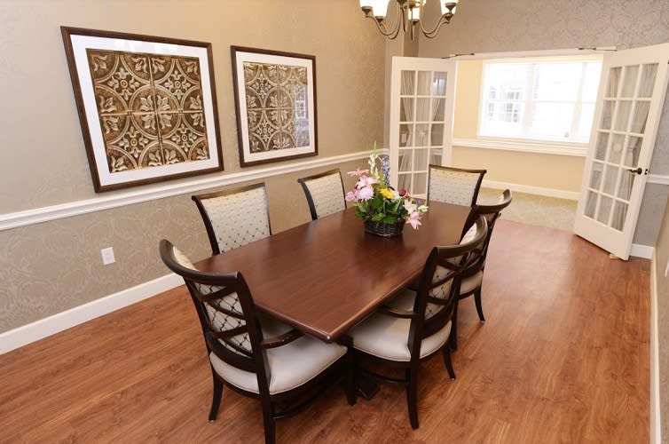 A well-decorated dining room featuring a wooden table with six chairs, framed artwork on the walls, and a hardwood floor.