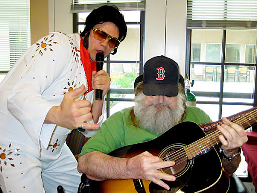 A lively music performance featuring a tribute artist and an audience member playing guitar.