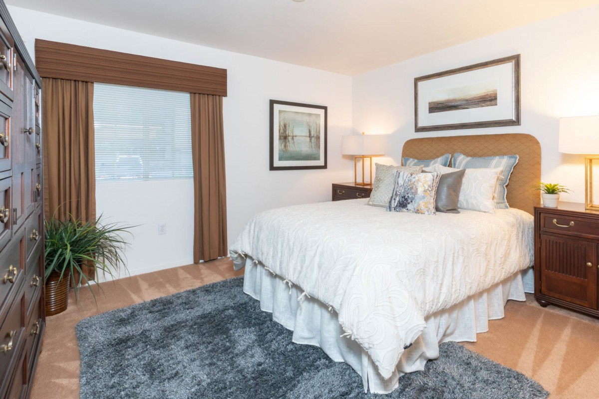 A cozy bedroom with a neatly made bed, artwork on the walls, and a plush carpet.