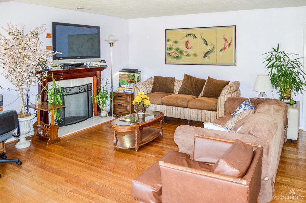 A cozy living room with a sofa, armchair, and fireplace, featuring elegant plants and artwork.