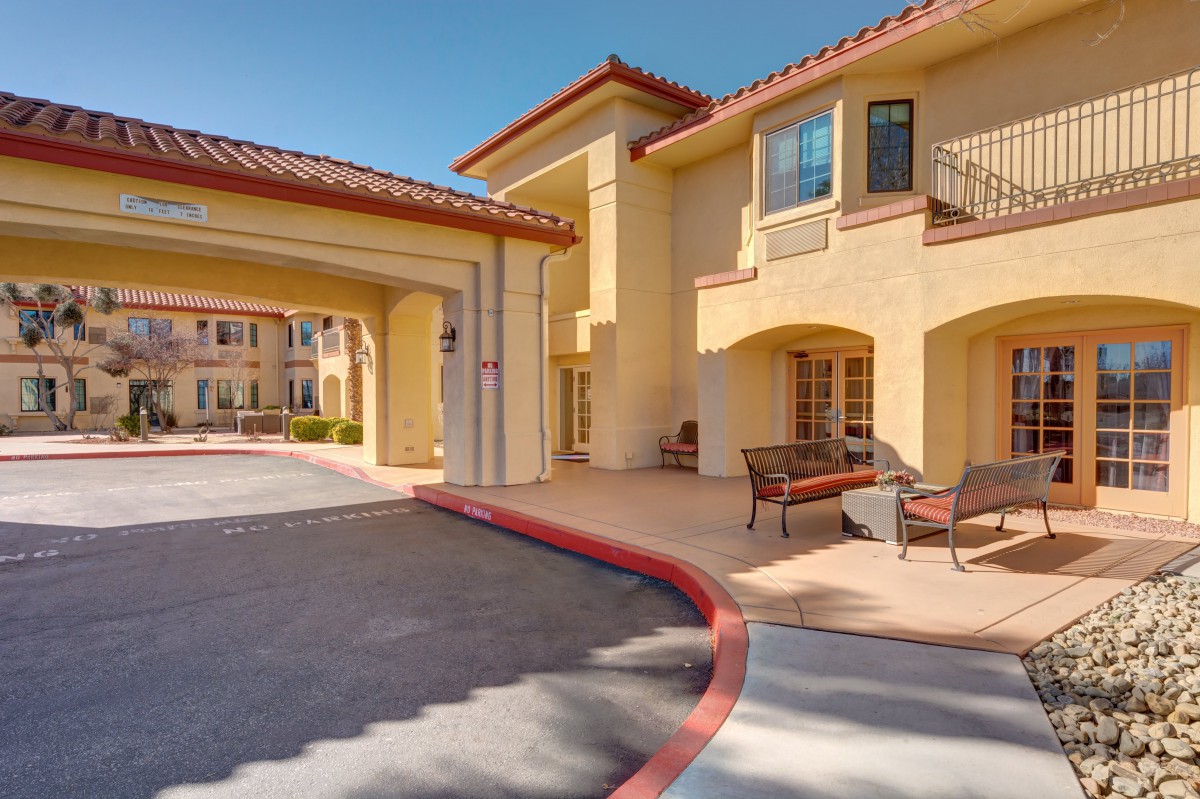 A Mediterranean-style residential building entrance with outdoor seating and a covered driveway.