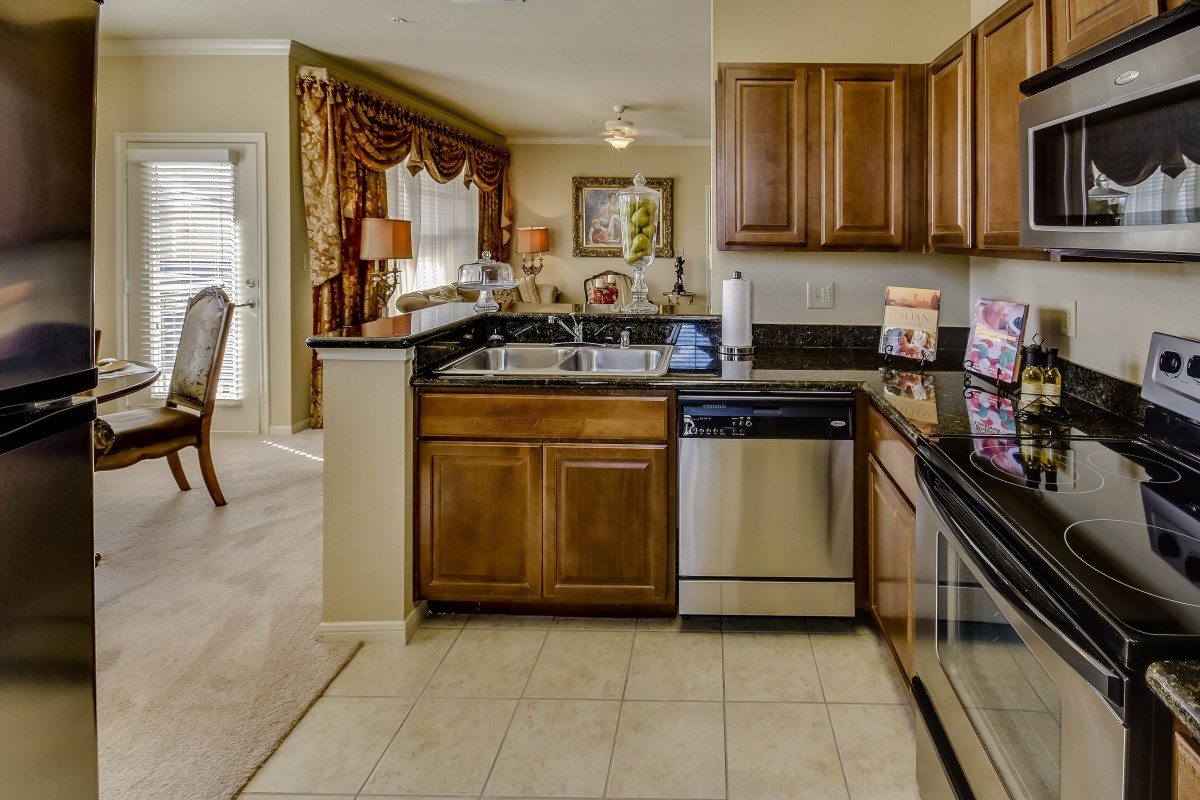 A modern kitchen with wooden cabinets, stainless steel appliances, and a tiled floor.