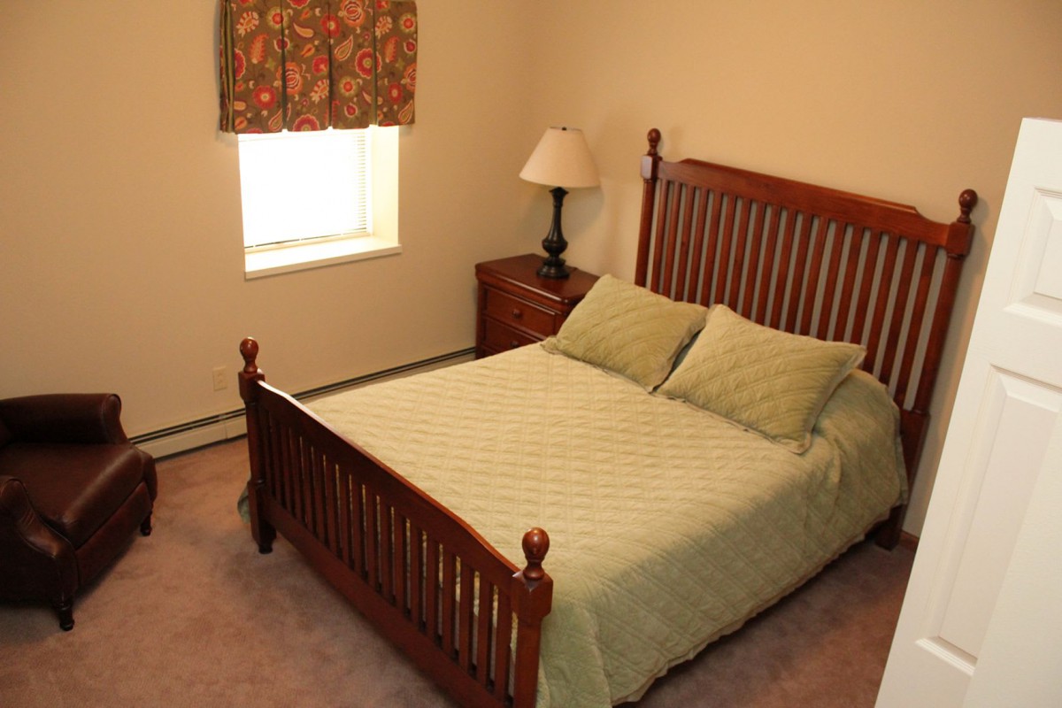 A cozy bedroom with a wooden bed frame, green bedding, and a nightstand with a lamp.