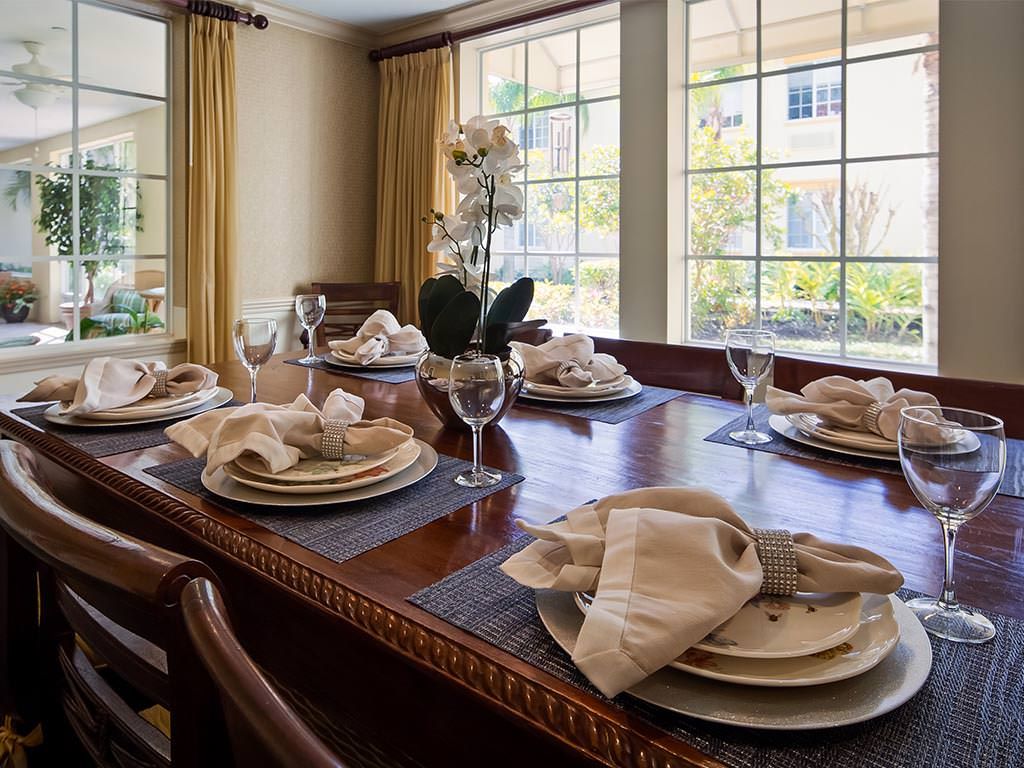 An elegantly set dining table in a sunlit room, adorned with flowers and neatly arranged napkins.