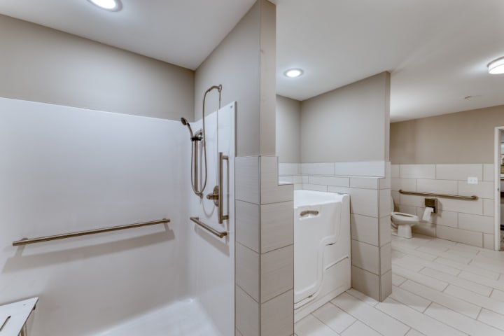 A modern bathroom featuring an accessible shower and a walk-in tub with grab bars and tile walls.
