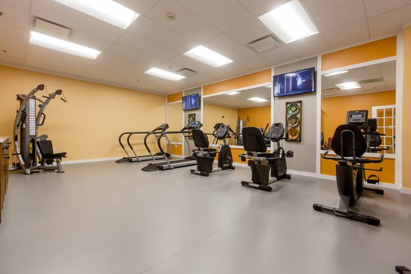 A well-lit gym with various fitness equipment including treadmills and stationary bikes.