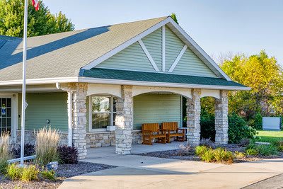A quaint house with a green facade and stone pillars surrounding the porch.