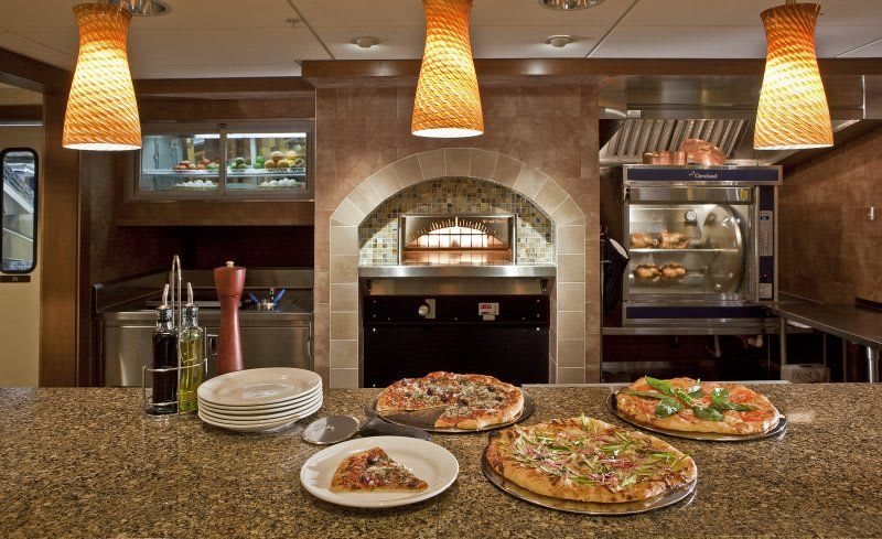A restaurant kitchen with pizzas displayed on the counter and a wood-fired oven in the background.