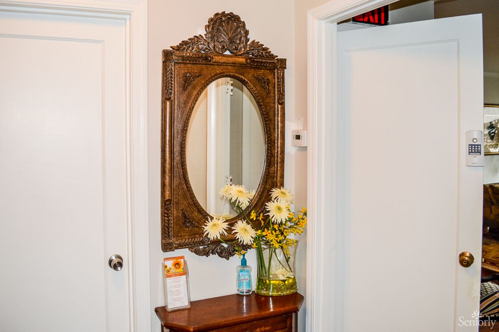 An elegantly decorated hallway featuring an antique mirror with a wooden frame and a floral arrangement.