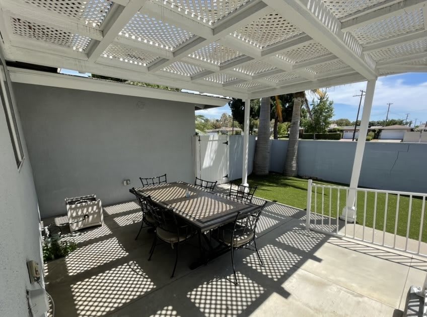 A sunny patio with a pergola casting intricate shadows over a dining table and chairs.